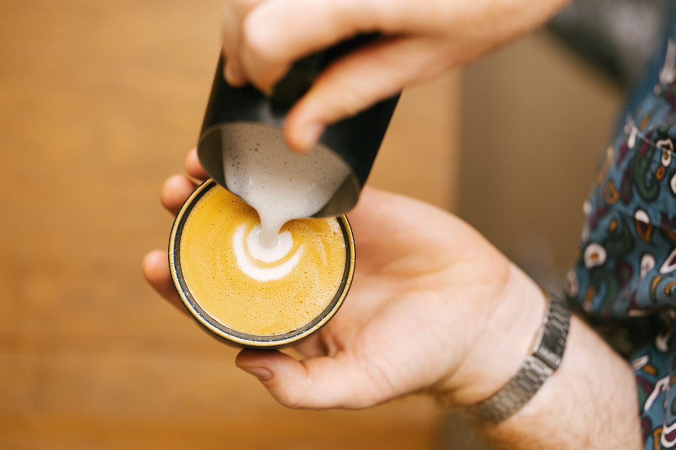 JoyBlast barista pouring steamed milk into a cappuccino held in hand